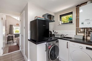 Une cuisine compacte équipée d’un lave-linge Bosch, d’un réfrigérateur noir et d’une fenêtre agrémentée d’une plante.