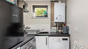 Une cuisine compacte équipée d’un réfrigérateur, d’un lave-linge et d’une fenêtre donnant sur un espace verdoyant.