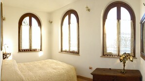 Un dormitorio con cama, cómoda y tres ventanas de arco.