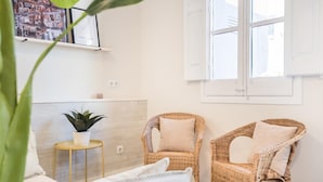 Ein Zimmer mit einem Bett, zwei Korbstühlen, einem kleinen Tisch mit einer Pflanze und einem Fenster mit weißen Fensterläden.