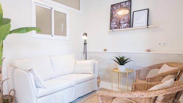 Ein weißes Sofa, Korbstühle, ein kleiner runder Tisch, ein Blumentopf und Wandbilder.