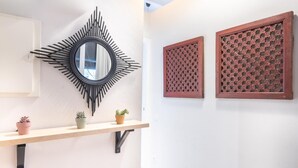 A wall with a black sunburst mirror, two wooden panels with intricate lattice designs, and a shelf with three potted plants. - Oasis with a sunny terrace in the heart of Gracia (Barcelona)