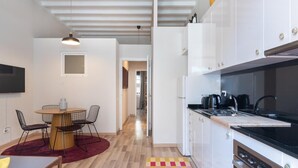 A modern kitchen with white cabinets, a black countertop, and a built-in oven. There is a dining area with a table and chairs, and a hallway leading to another room. - Oasis with a sunny terrace in the heart of Gracia (Barcelona)