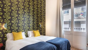 A hotel room with a bed, two pillows, a nightstand, a red chair, and a window with a view of the outside. - Oasis with a sunny terrace in the heart of Gracia (Barcelona)