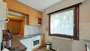 Eine kleine Küche mit Holzschränken, einem eingebauten Ofen, einem Fenster mit Vorhängen und einer Heizung.