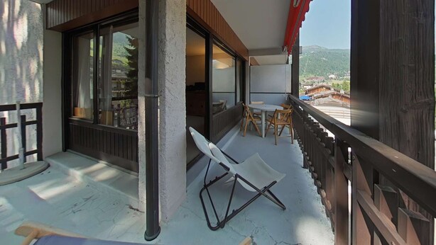Ein Balkon mit Tisch und Stühlen, Blick auf eine gebirgige Landschaft und ein rotes Markisen