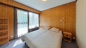 Ein Schlafzimmer mit Holzwandverkleidung, einem großen Bett, einem Nachttisch und einem Fenster mit Vorhängen.