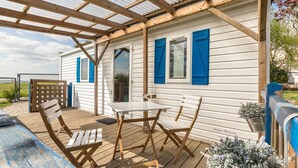 Un espacio al aire libre cubierto con una mesa y sillas, una terraza de madera y una casa con contraventanas azules.