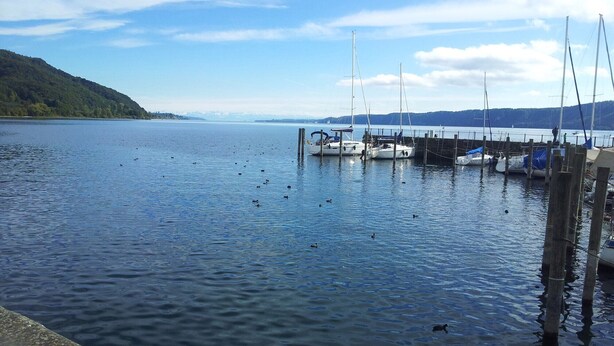Un lago tranquilo con barcos amarrados a un muelle, rodeado de colinas.