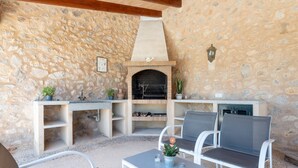 Un patio al aire libre con muros de piedra, una chimenea de ladrillo, muebles blancos y plantas en macetas.
