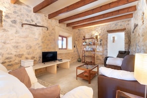 A cozy living room with stone walls, wooden beams, a television, a bookshelf, and a comfortable sofa.
