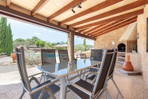 An outdoor patio with a glass table and chairs, a stone wall, and a view of the surrounding landscape.