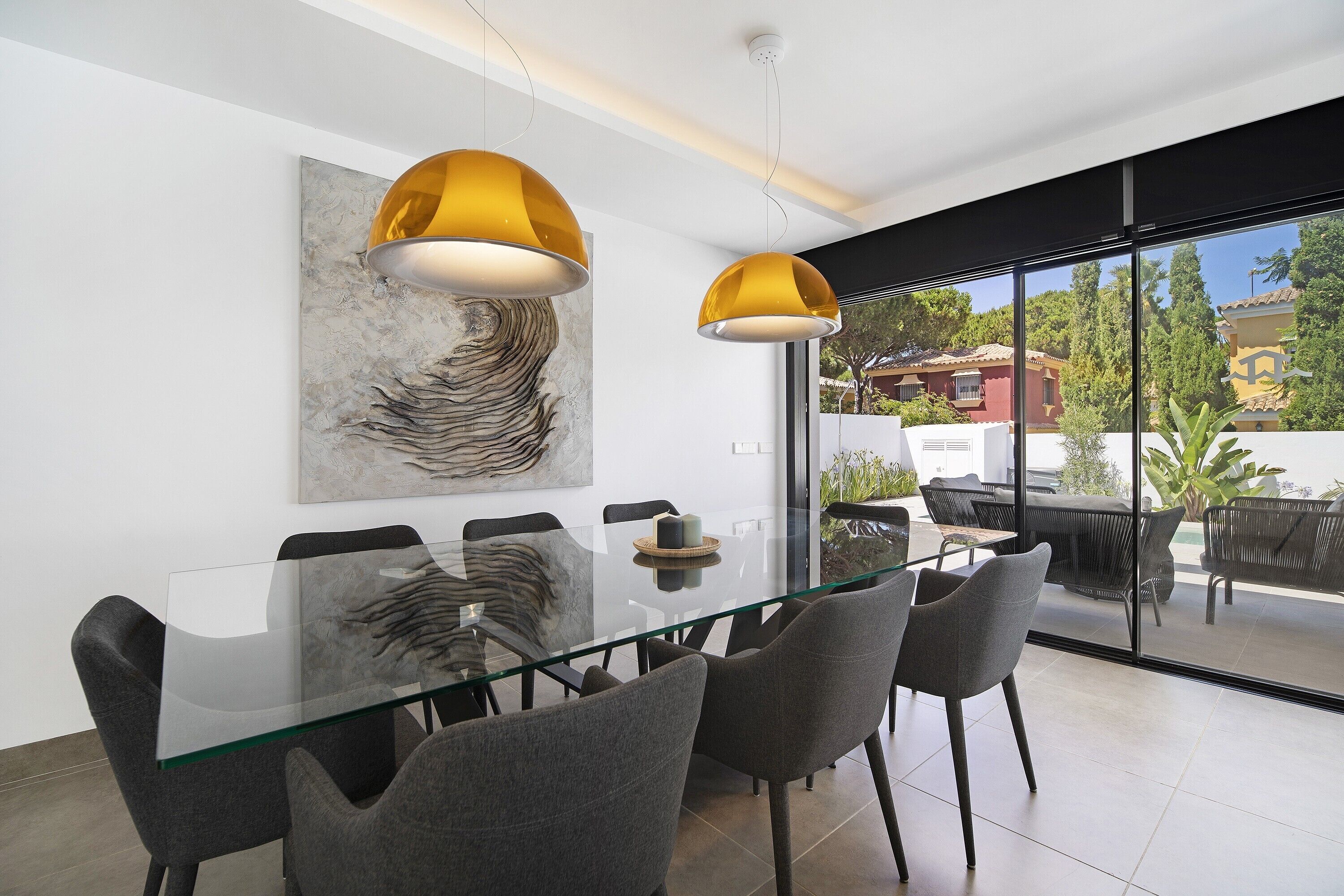 Un espace repas moderne avec une table en verre, des chaises grises et un grand tableau abstrait accroché au mur.