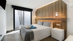 Une chambre moderne avec un grand lit, des tables de chevet, un mur d’accent en bois et une vue à travers une porte coulissante.