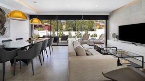 Un salon moderne comprenant un canapé, une table à manger et des chaises, un téléviseur et un balcon aménagé avec du mobilier d’extérieur.
