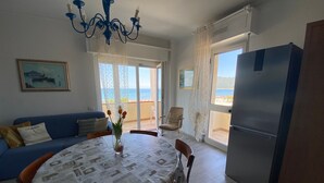A dining area with a table, chairs, a chandelier, a sofa, and a view of the sea through large windows.