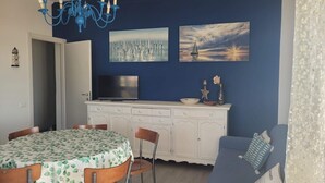 A dining area with a table, chairs, a TV, and a blue wall with artwork.