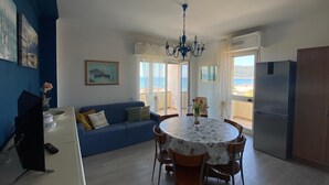 A living room with a sofa, dining table, chairs, a chandelier, and a refrigerator.