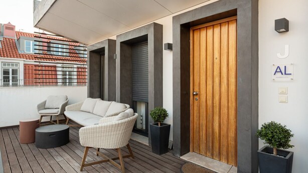 A modern outdoor seating area with wicker furniture, a wooden door, and potted plants. - JOIVY Spacious flat in Bairro Alto (Lisboa)