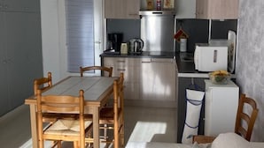 Kompakti keittiö, jossa on puiset kaapit, ruokapöytä tuoleineen ja jääkaappi.
