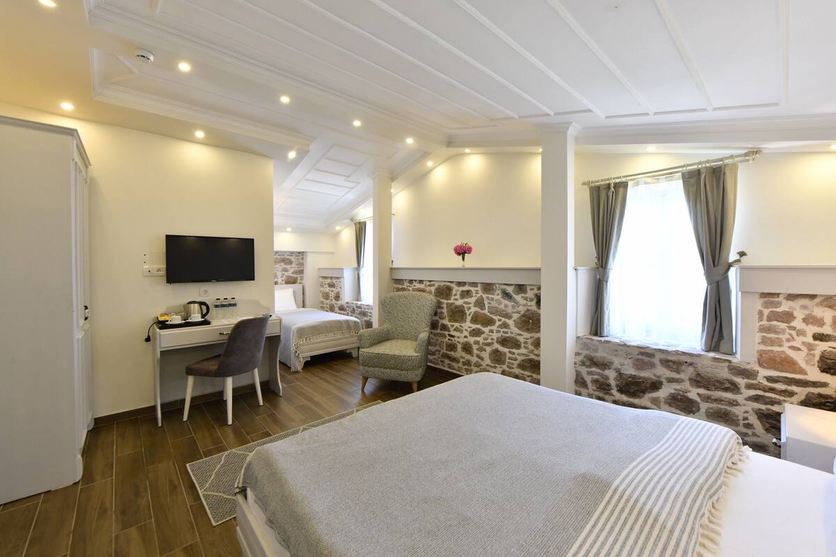 Ein Schlafzimmer mit Bett, Schreibtisch, Stuhl, Fernseher und einer Steinwand.