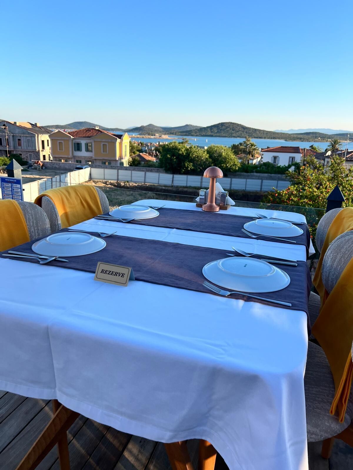 Une table dressée pour six personnes, avec un marque-place indiquant « RÉSERVÉ », sur une terrasse donnant sur une ville côtière.