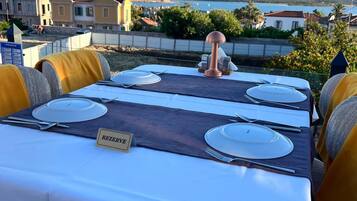 Une table dressée pour six personnes, avec un marque-place indiquant « RÉSERVÉ », sur une terrasse donnant sur une ville côtière.