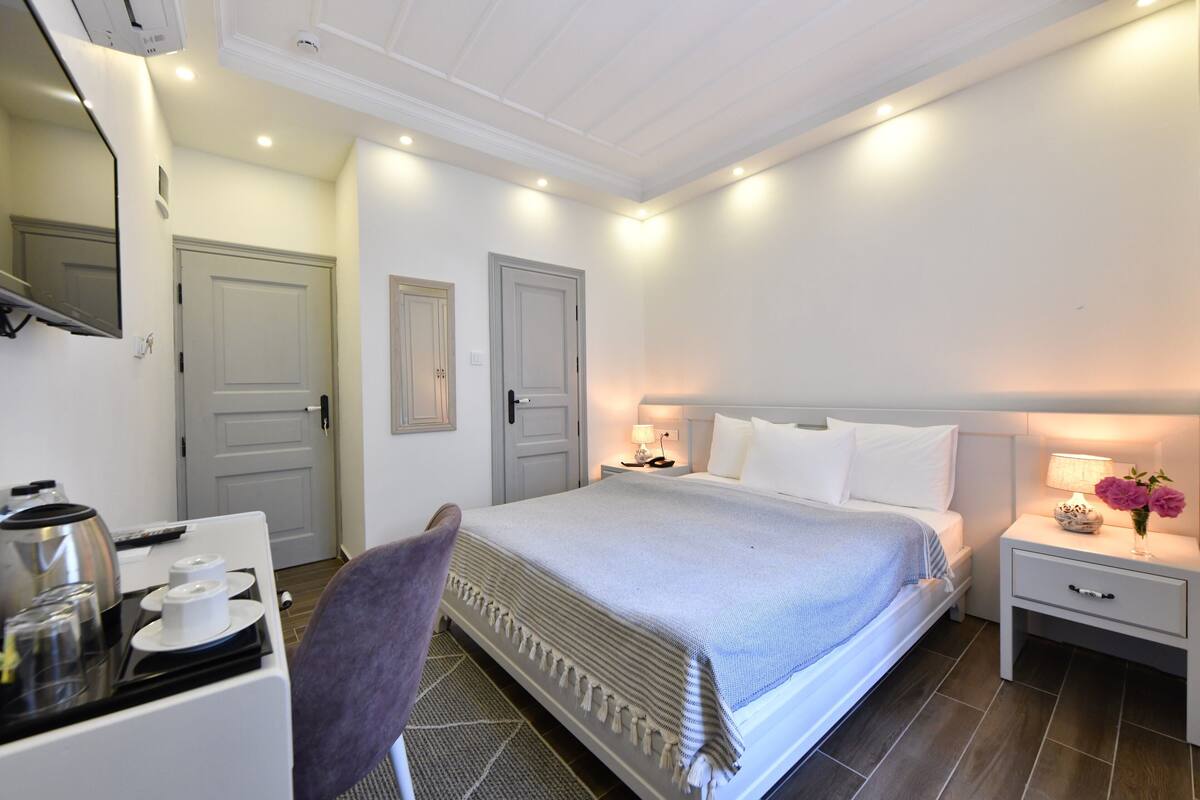 Ein Hotelzimmer mit Bett, Nachttisch, Stuhl und Schreibtisch, inklusive Wasserkocher und Tassen.