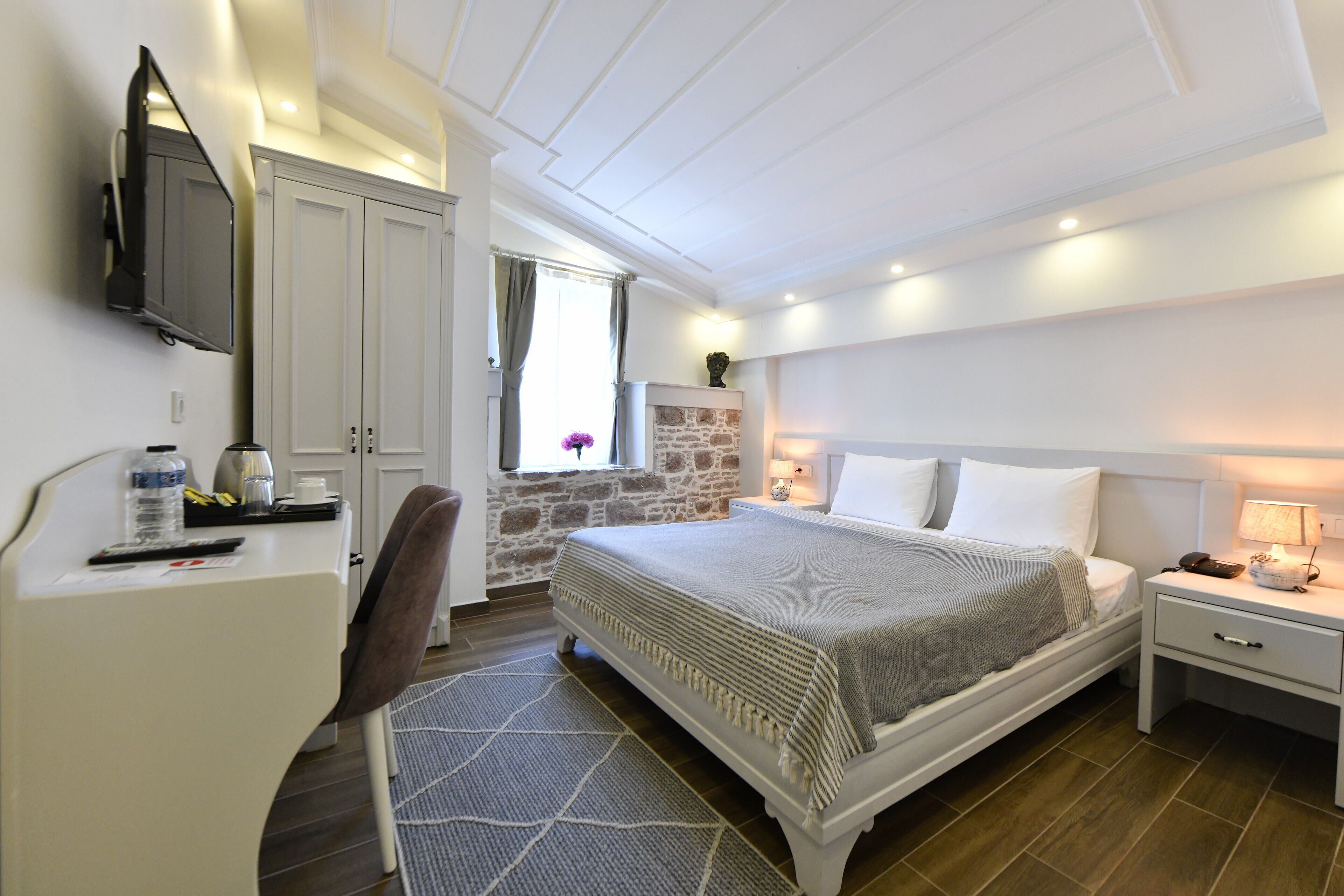 Une chambre à coucher comprenant un lit, une table de chevet, une lampe, un téléviseur fixé au mur et un bureau avec une chaise.