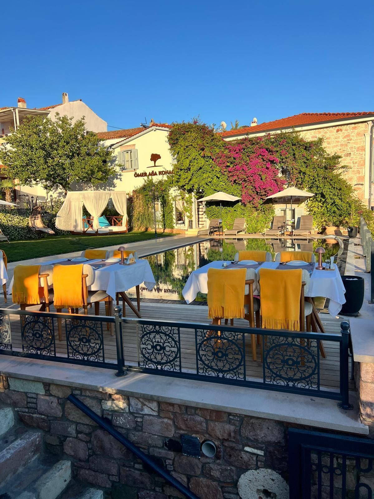 An outdoor dining area with tables and chairs, a pool, and a stone wall.