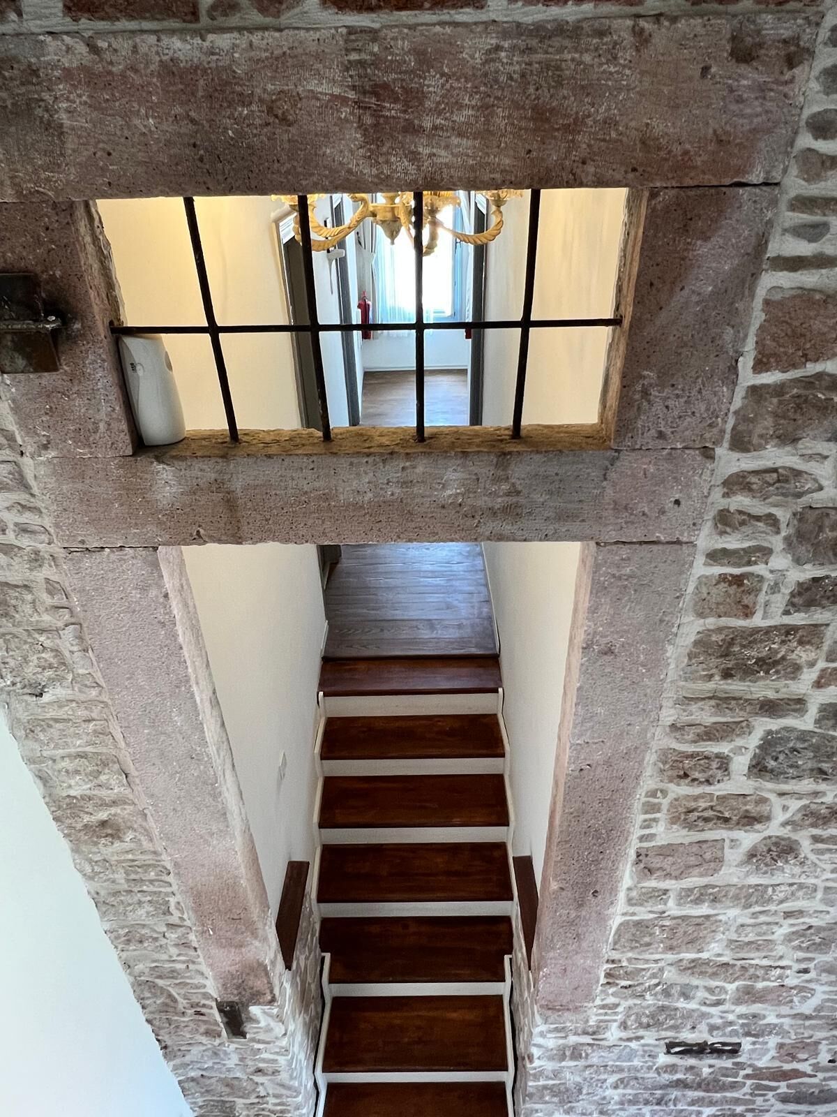 A staircase with stone walls and a wooden floor leading to a second-floor balcony with a view of the interior.