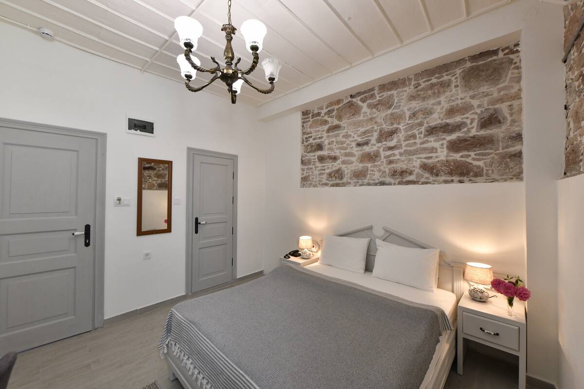 Ein Schlafzimmer mit einem großen Bett, zwei Nachttischen, einer Chandelieber, einer Steinwand und einer Tür.