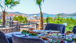 A table set for a meal with various dishes and drinks, overlooking a scenic view of a coastal area. - Omer Aga Konagi (Ayvalik)