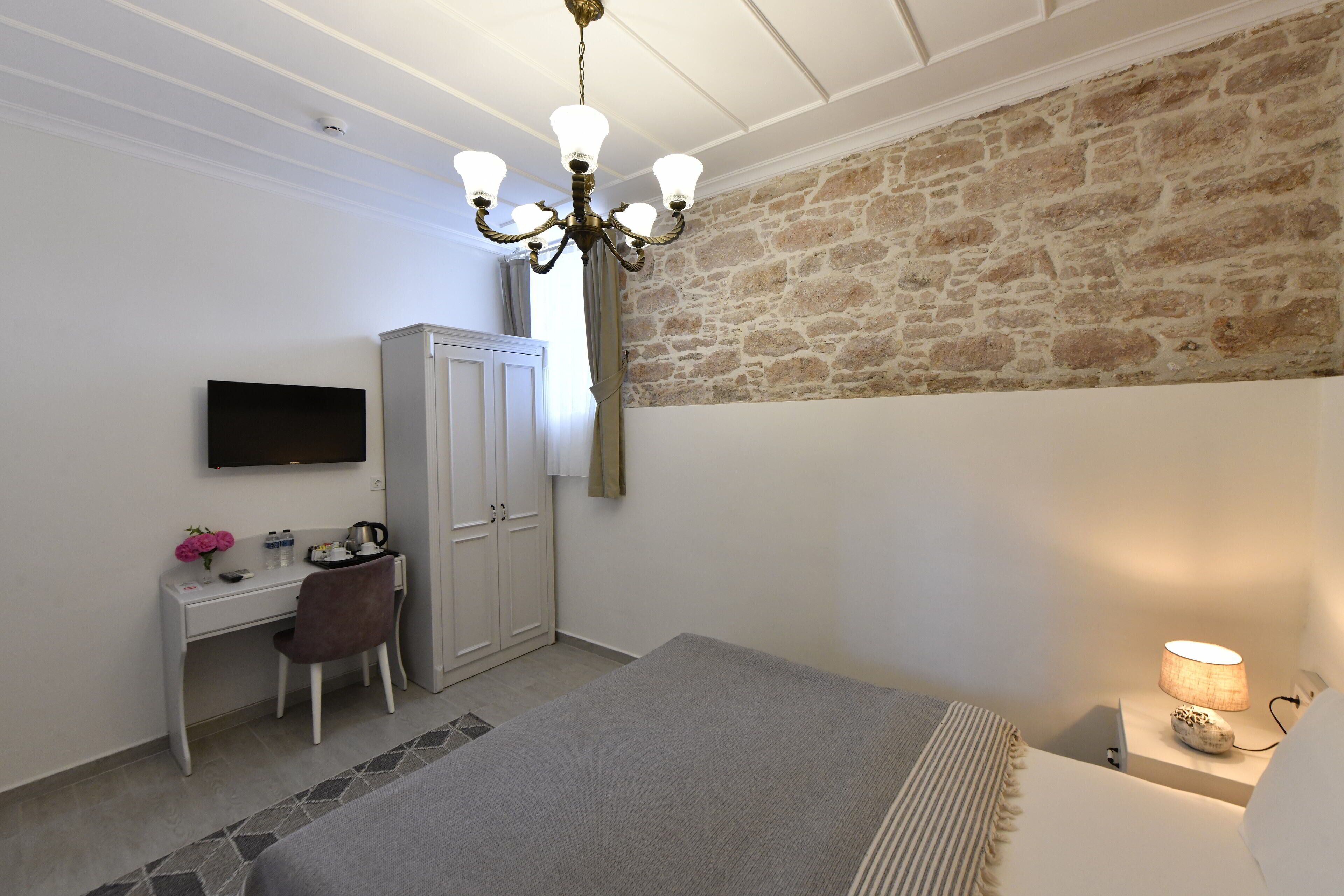 Un dormitorio con cama, escritorio, televisión, armario y pared de piedra.