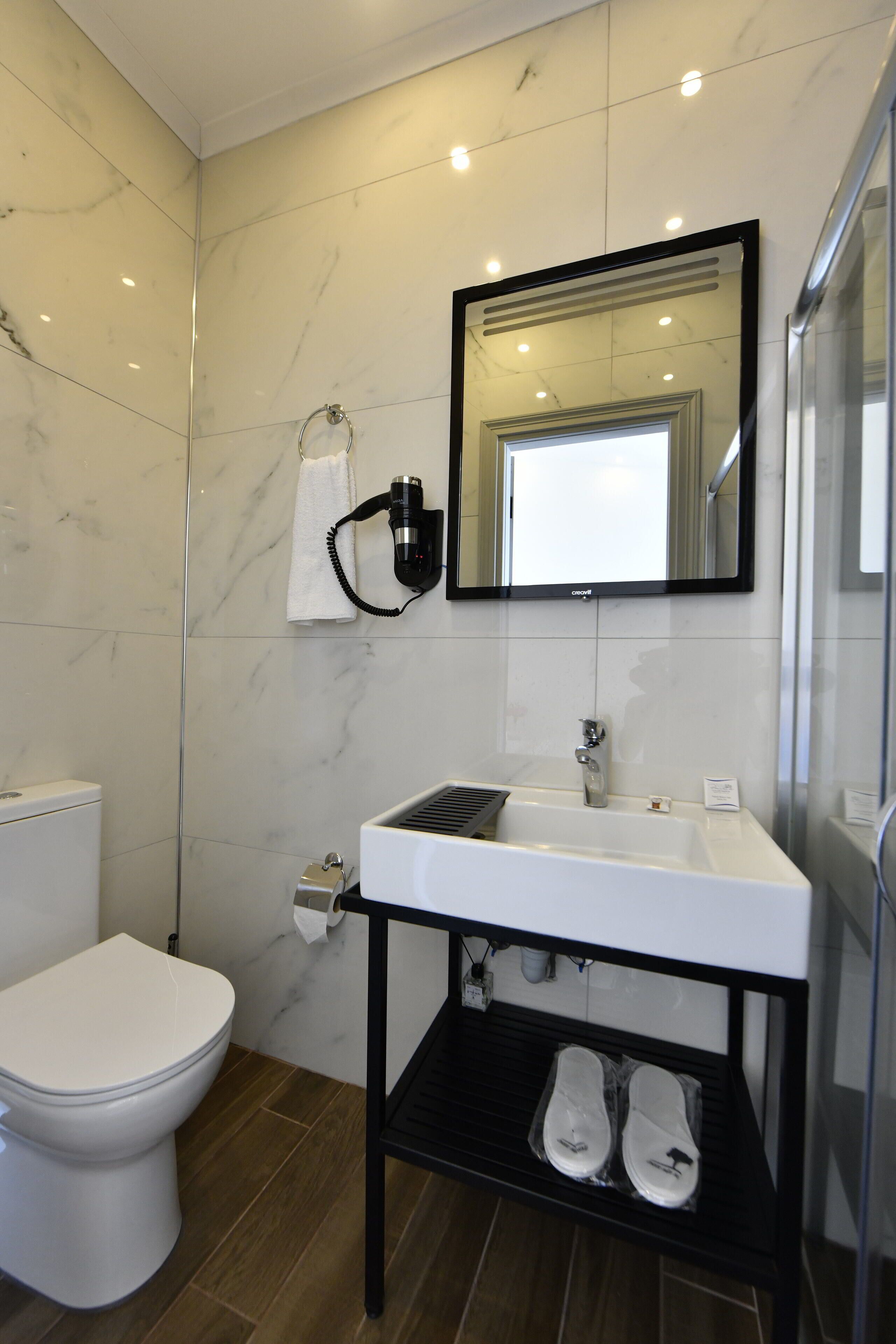 Ein modernes Badezimmer mit einer weißen Toilette, einem Waschbecken mit Ablagefläche in Schwarz und einem Spiegel darüber.