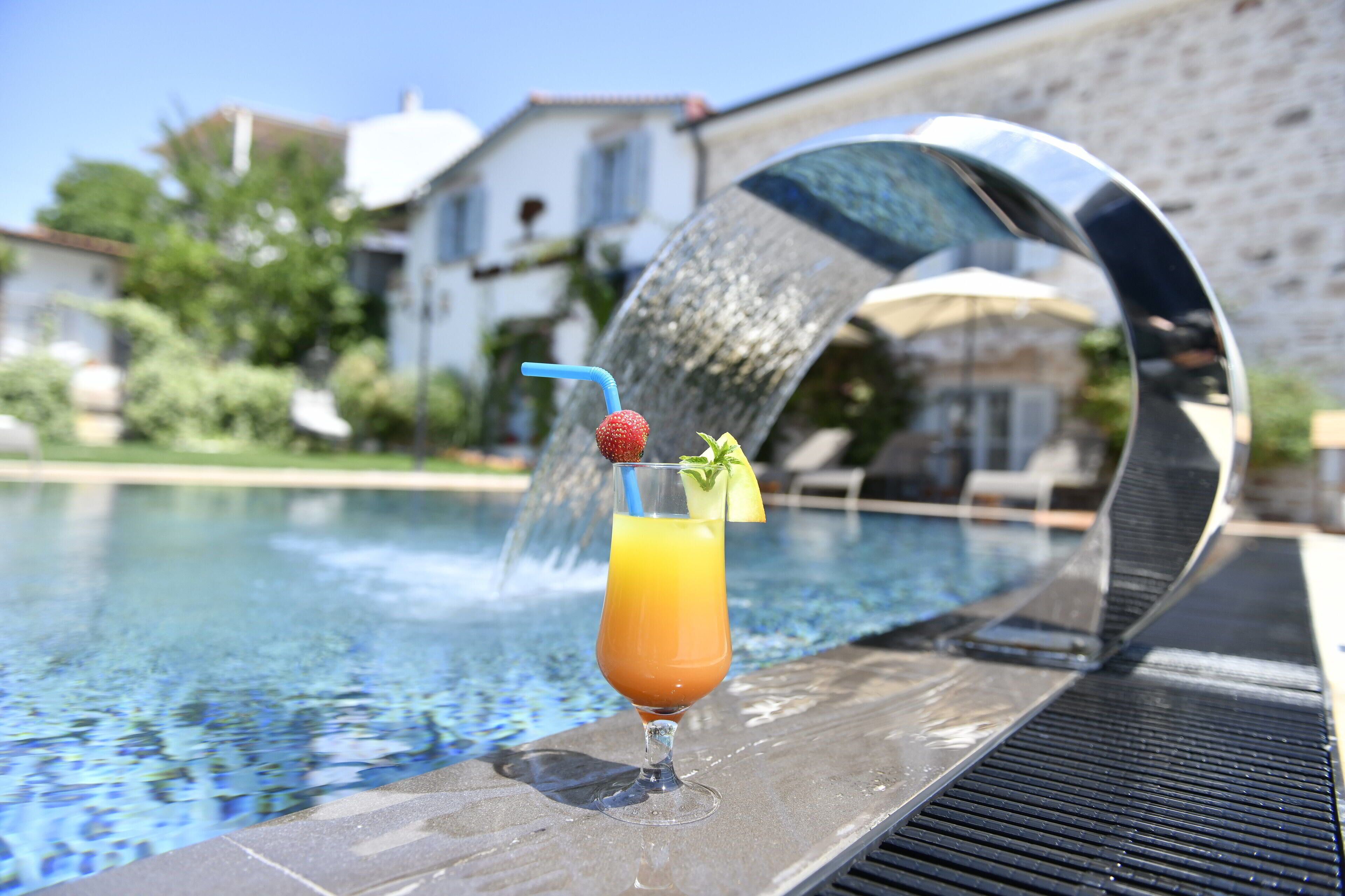 A glass of orange juice with a strawberry and mint garnish on a poolside table.
