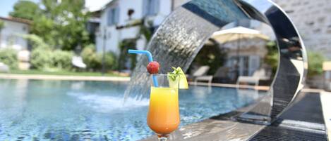 A glass of orange juice with a strawberry and mint garnish on a poolside table.
