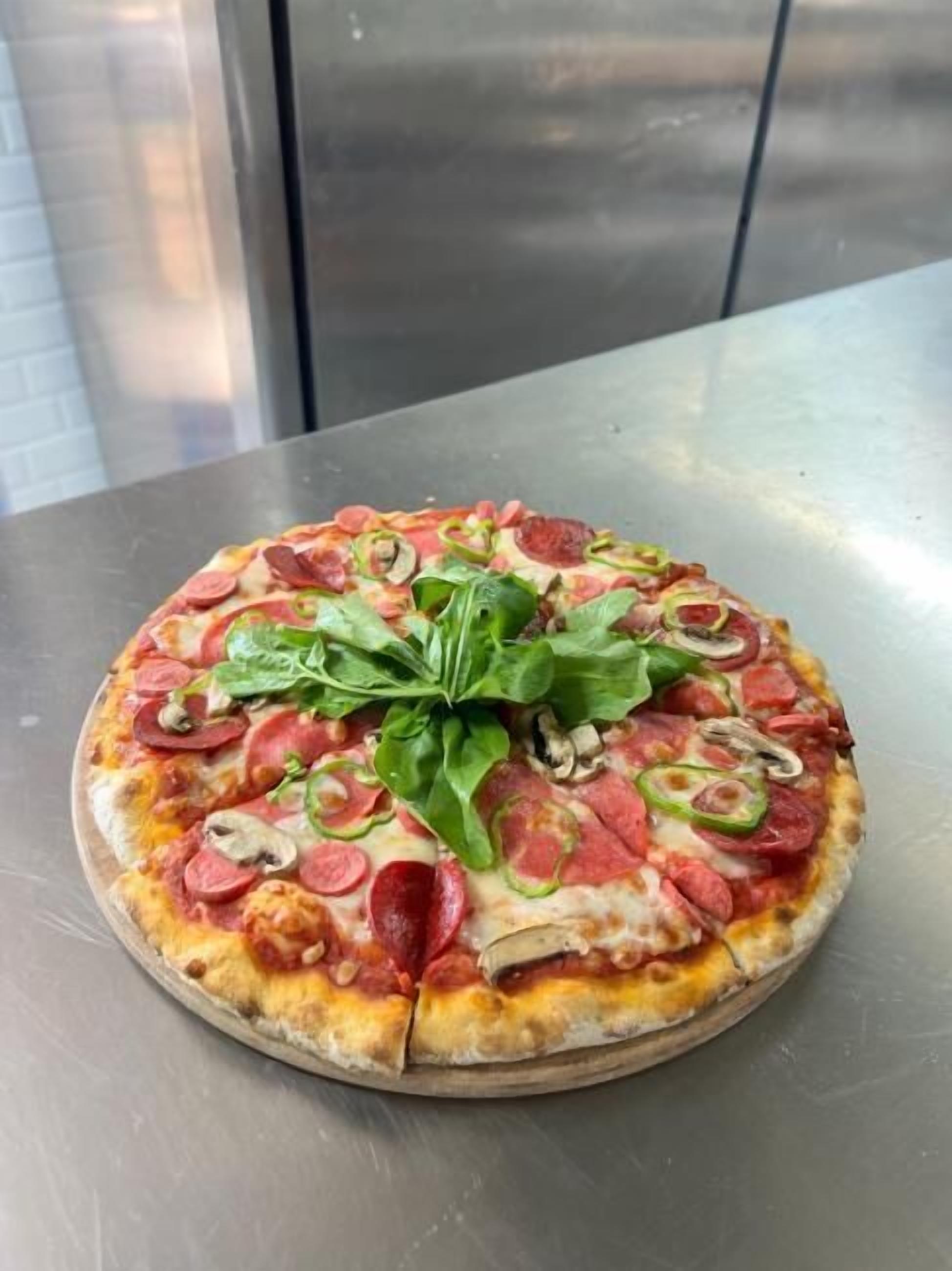 Pizza met pepperoni, champignons en spinazie op een metalen ondergrond.