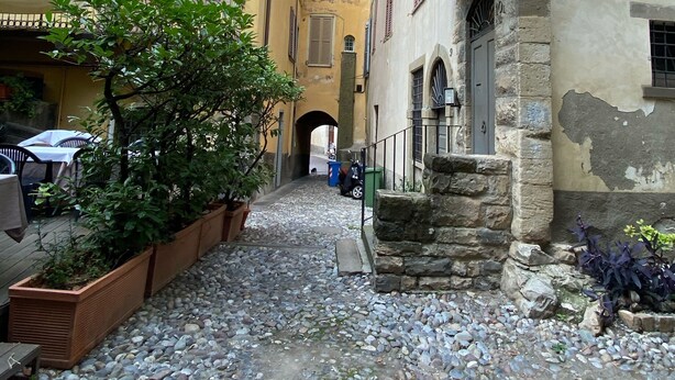 Un callejón estrecho con pavimento de adoquines, muros de piedra y edificios tradicionales con contraventanas.