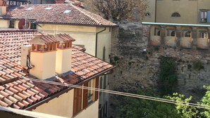Vista de un edificio con techos de tejas de terracota, un muro de piedra y un árbol en primer plano.