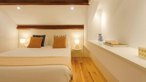 A bedroom with a bed, bedside lamps, a nightstand, and a shelf with books and a vase. - Vitoria Duplex Apartment by DA'HOME (Porto)