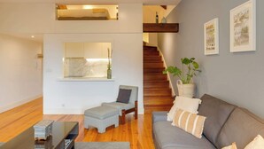 A modern living room with a wooden staircase, a grey sofa, a small table, and a bench. - Vitoria Duplex Apartment by DA'HOME (Porto)