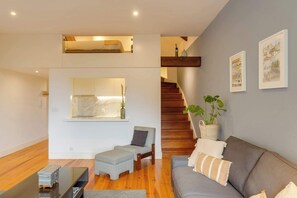 A modern living room with a wooden staircase, a grey sofa, a small table, and a bench. - Vitoria Duplex Apartment by DA'HOME (Porto)