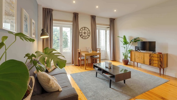 A living room with a sofa, coffee table, dining table, chairs, curtains, a clock, a TV, and potted plants. - Vitoria Duplex Apartment by DA'HOME (Porto)