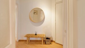 Un pasillo con un banco de madera, un espejo redondo en la pared y una cesta de mimbre en el suelo.