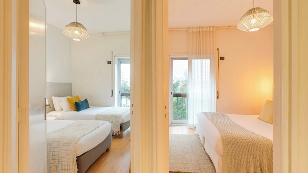 Un dormitorio moderno con dos camas, un ventanal grande y un balcón.