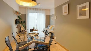 Una sala de estar moderna con una mesa de comedor de vidrio, sillas negras, un sofá y un ventanal con cortinas ligeras.