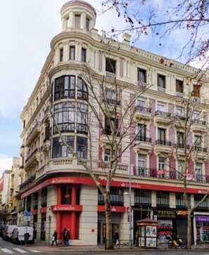 A multi-story building with a classic architectural style, featuring a corner entrance with a red awning and a visible storefront with a sign that reads "Santander".