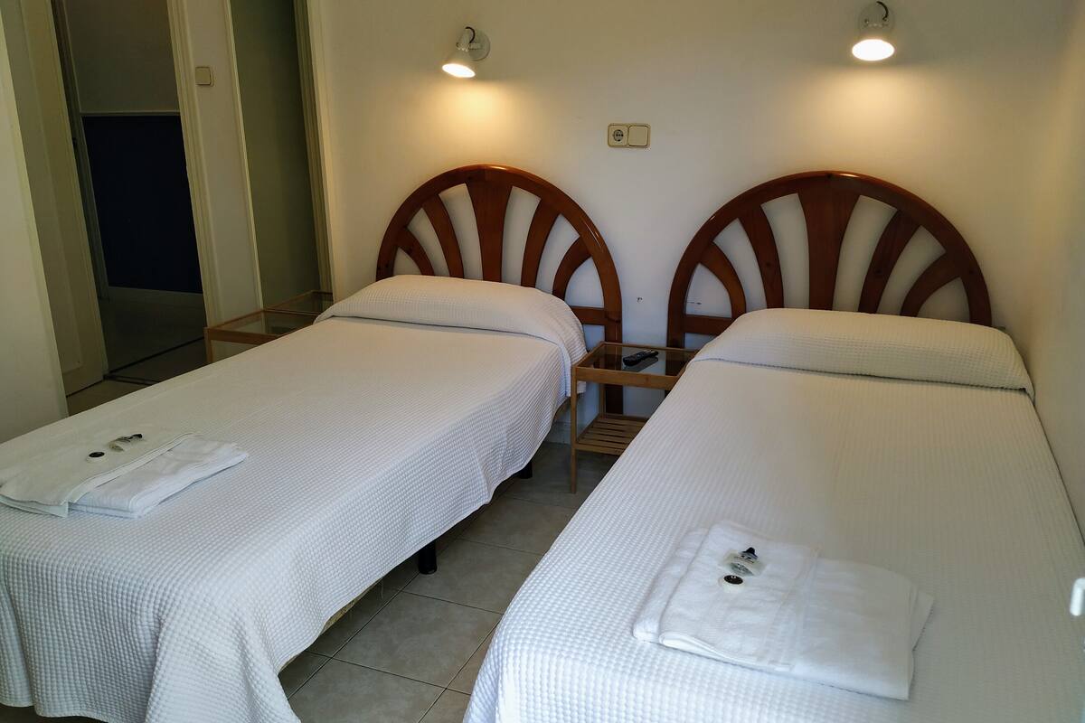 Two single beds with wooden headboards, a bedside table with a remote control, and a wall socket.
