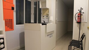 Un mostrador de recepción con encimera blanca, un extintor en la pared y una silla negra a la derecha.